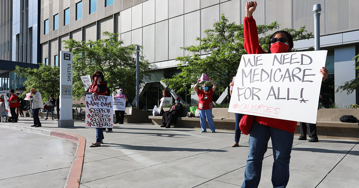 Nurse raising fist and holding sign "We need Medicare For All!"