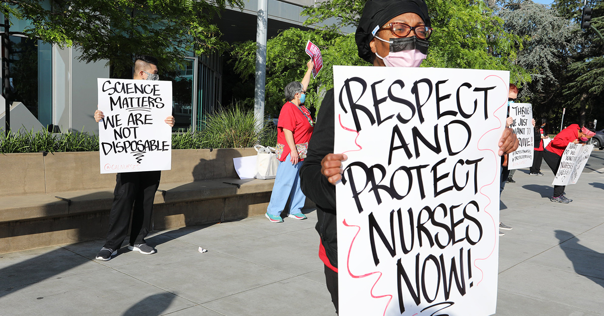 Nurses outside facility with signs "Respect and protect nurses now!" and "Science matters, we are not disposable"