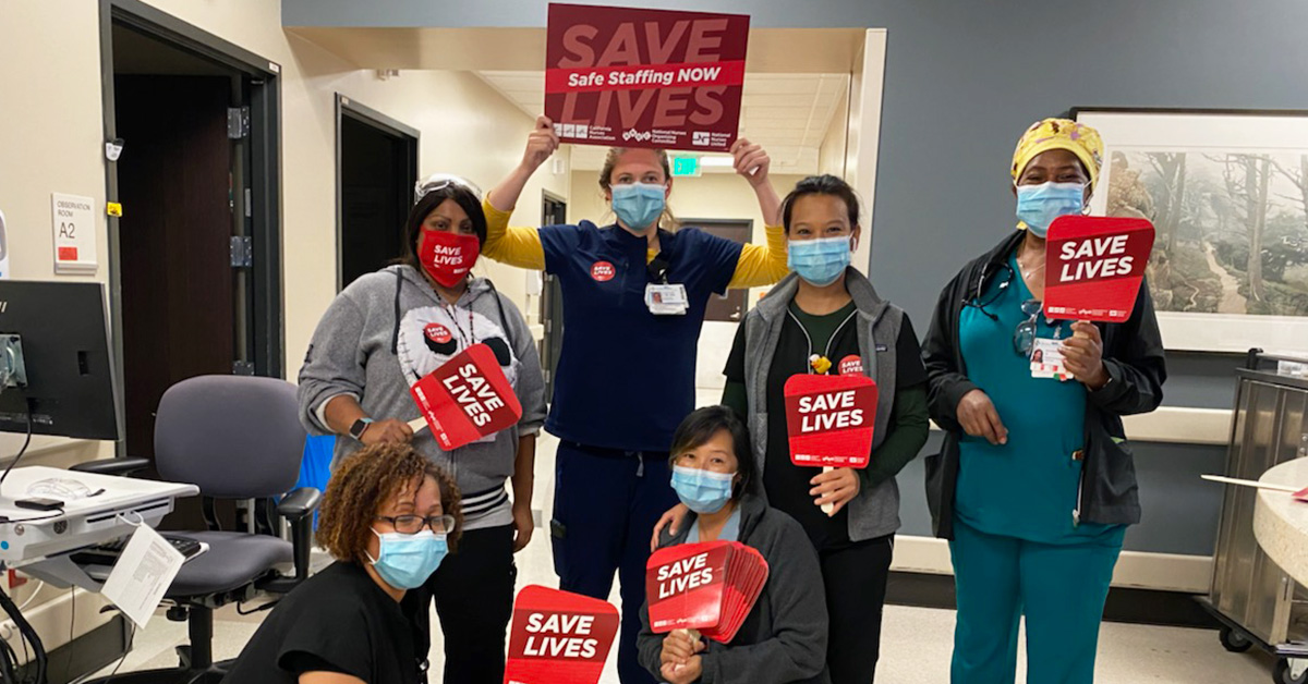 Group of four nurses inside hospital hold signs "Safe Staffing Now", "Save Lives"
