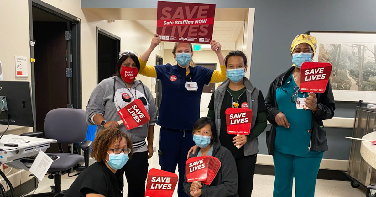 Group of four nurses inside hospital hold signs "Safe Staffing Now", "Save Lives"