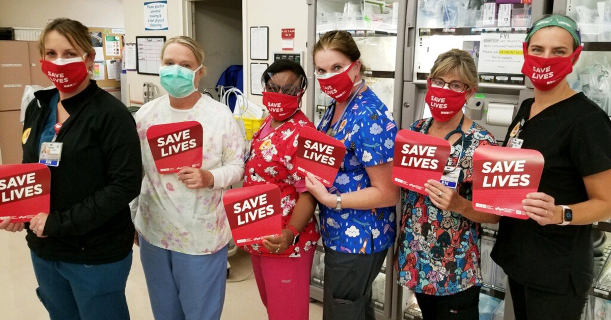 Nurses in hospital room holding "Save lives" signs