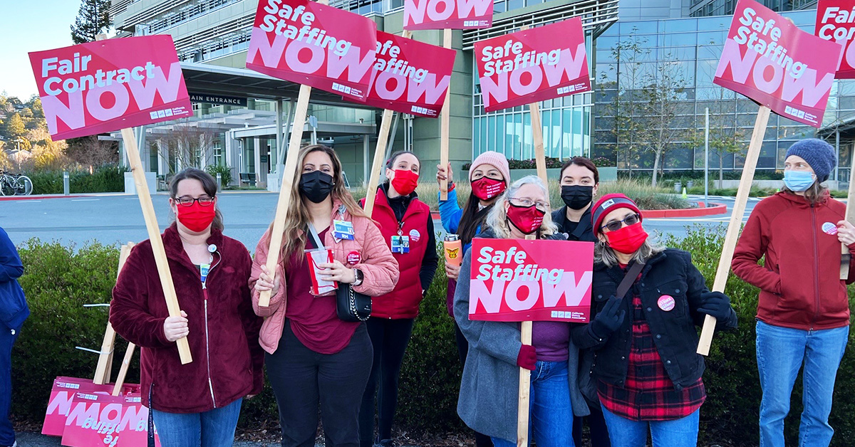 Group of nurses outside hold signs calling for safe staffing