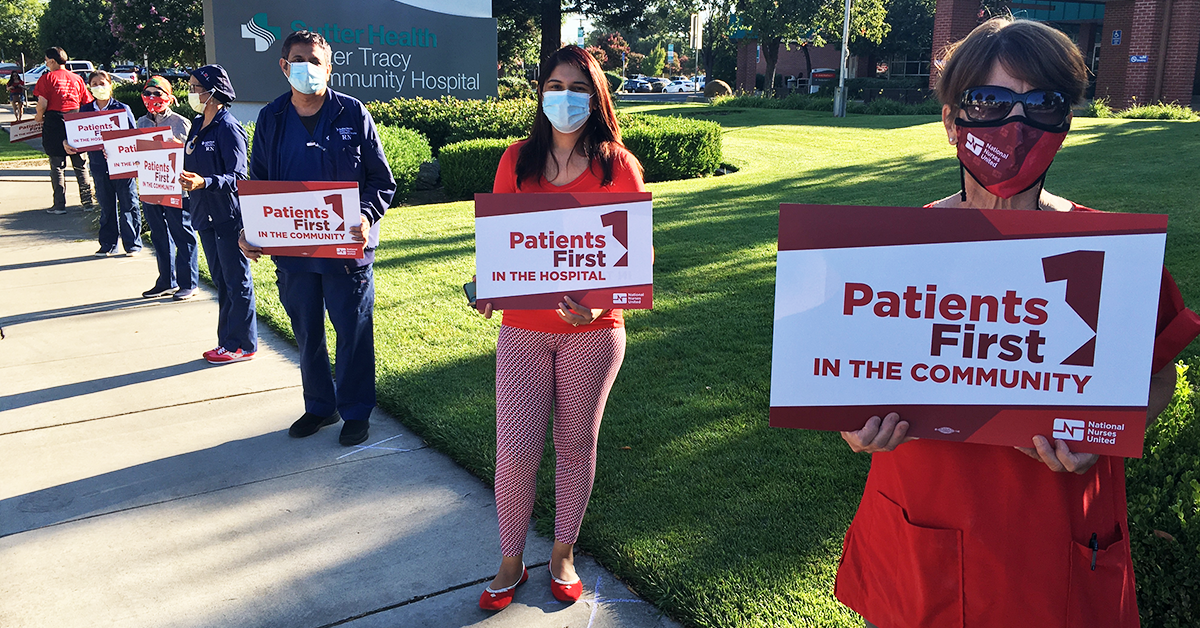Nurses holding signs outside hospital "Patients first in the community"
