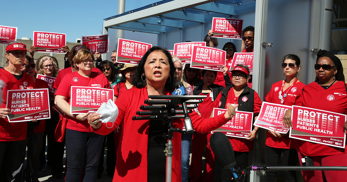 Bonnie Castillo, RN, Executive Director of NNU at podium surrounded by nurses holding signs "Protect Nurses, Patients, Public Health"