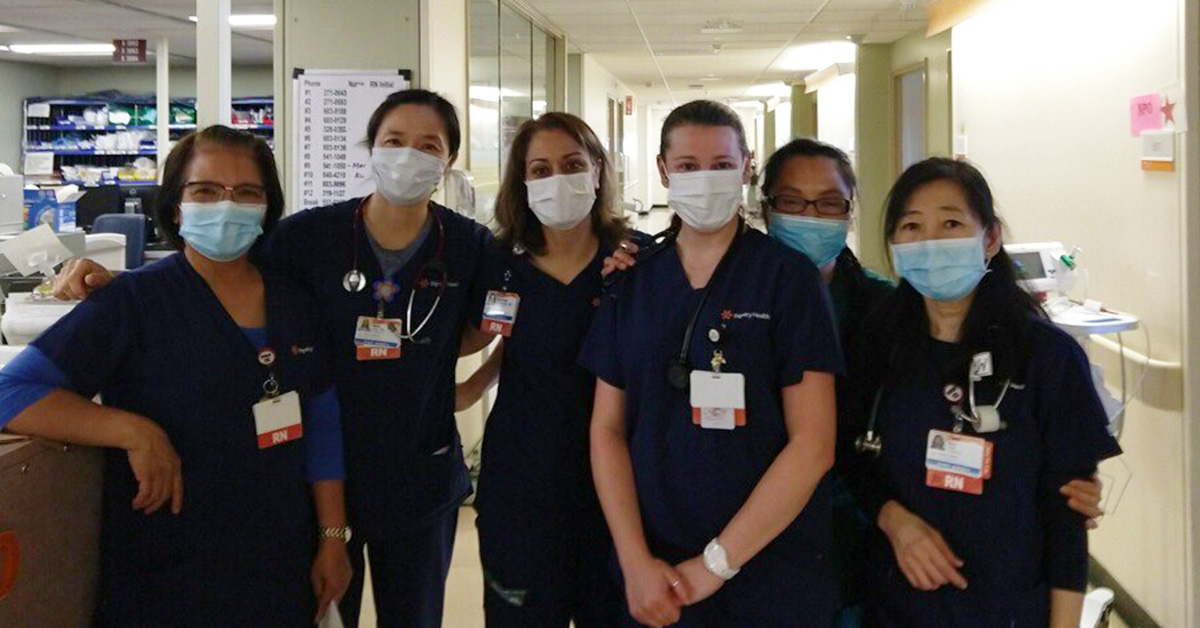 Group of six nurses arm-in-arm in hospital hallway