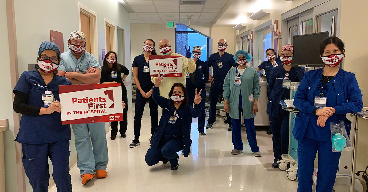 Large group of nurses in hospital hallway, two hold signs "Patients First"