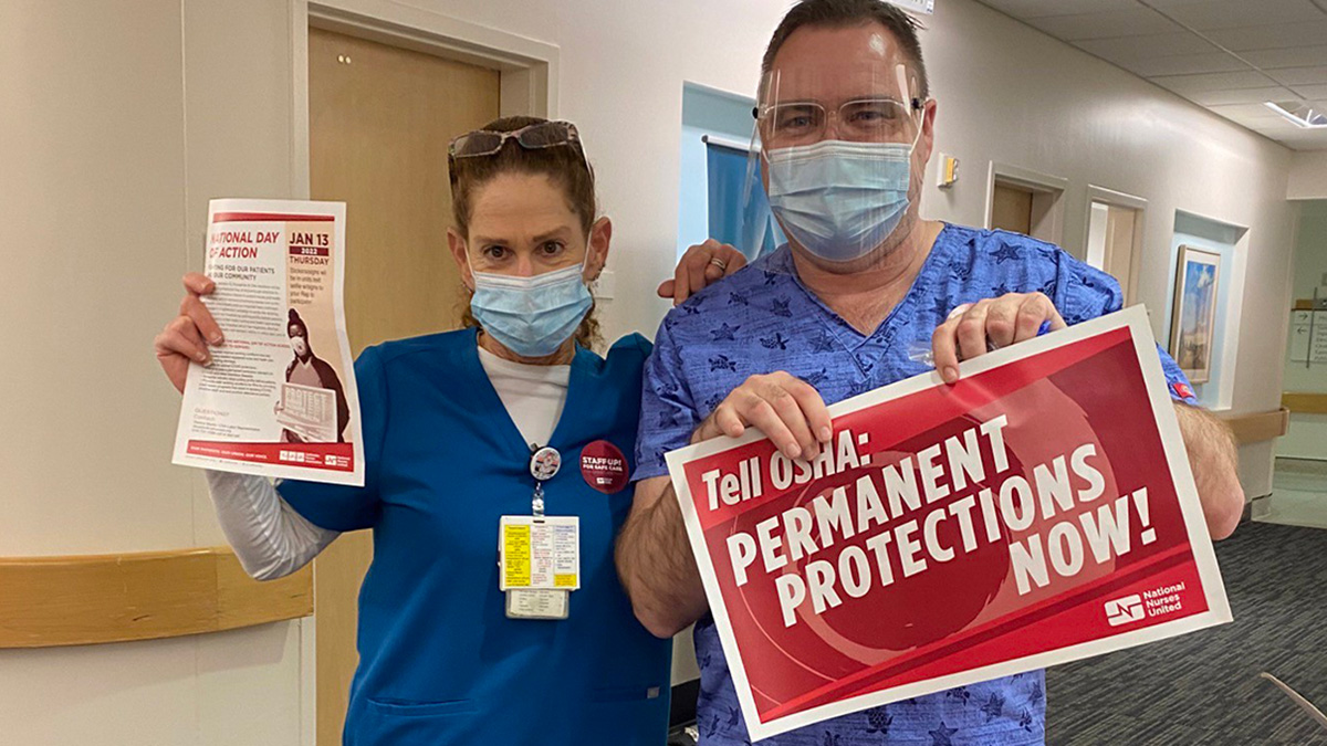 Two nurses inside hospital hold signs calling for permanent ETS