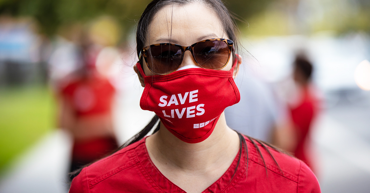 Nurse in sunglasses wearing mask which says "Save lives"