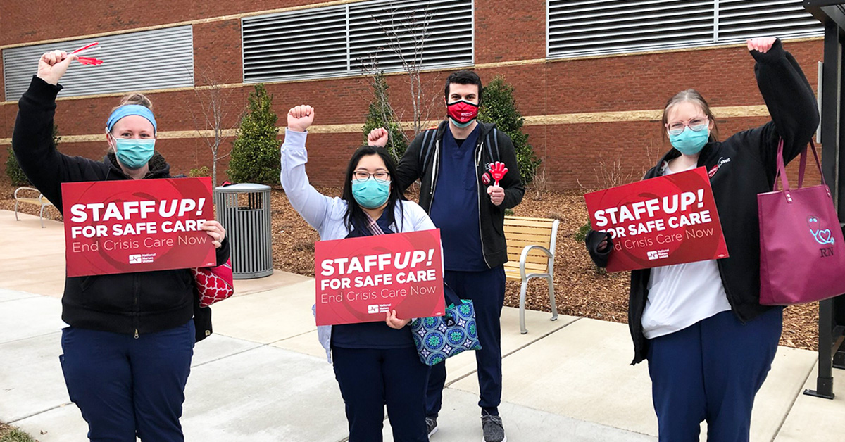 Nurses outside hospital hold signs "Staff Up for Safe Care"