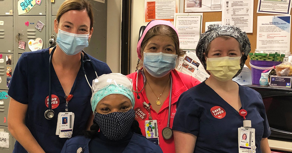 Group of four nurses inside hospital wearing stickers saying "Save Lives"