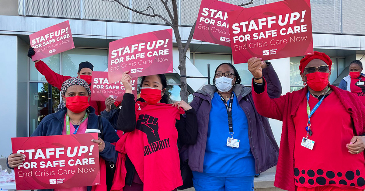 Group of nurses outside hold signs "Staff up for safe patient care"