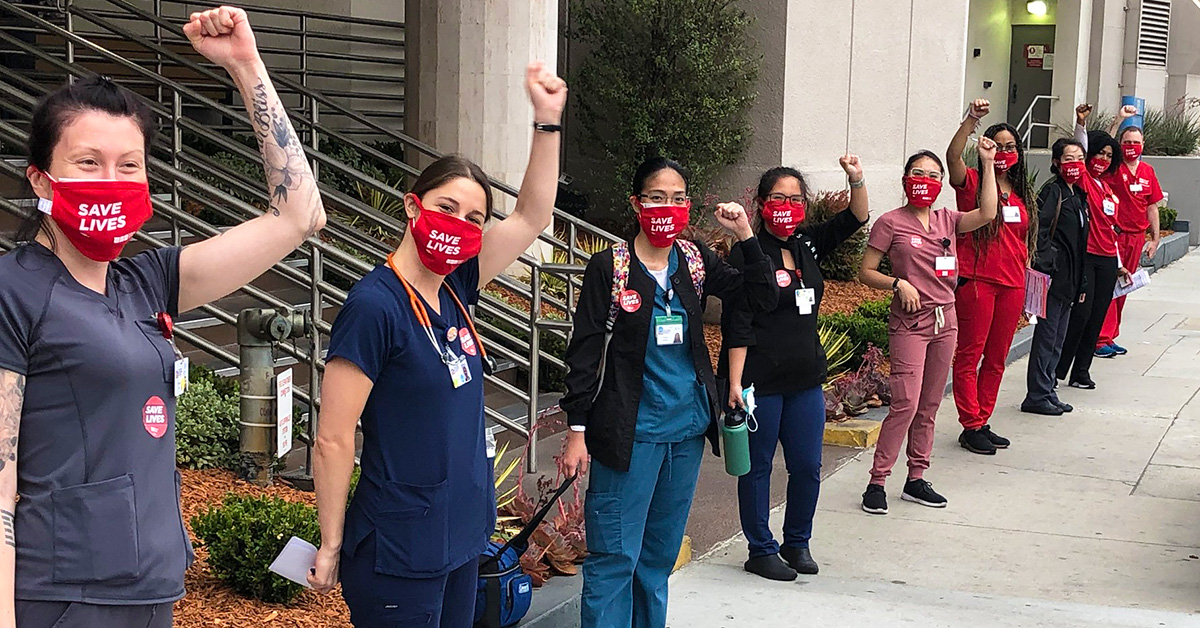 Group of nurses outside hospital with raised fists