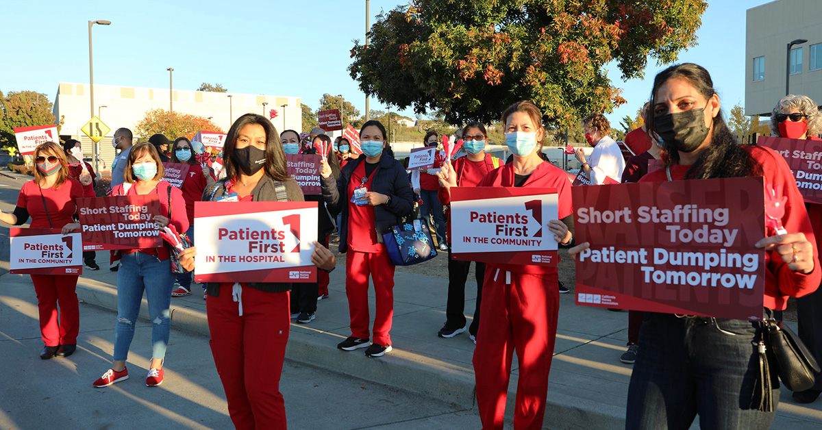 Large group of nurses outside hold signs "Patients First"