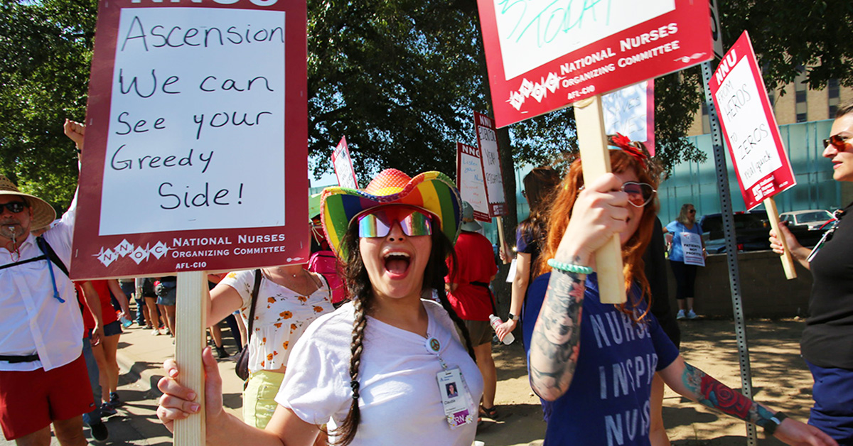 Nurses on picket line, one holds sign "Ascension, we can see your greedy side"