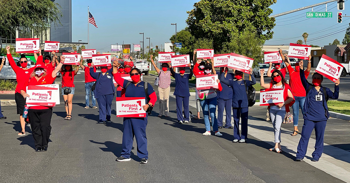 Large group of nurses outside hospital holding signs "Patients First"