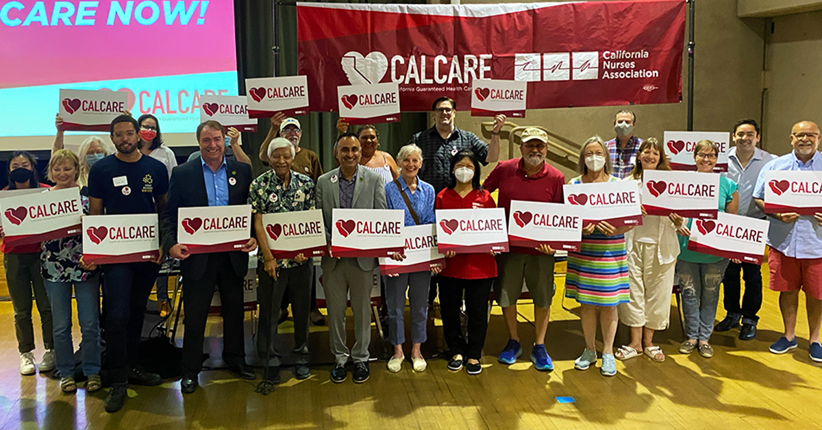 Large group of people standing in front of CalCare banner, holding CalCare signs