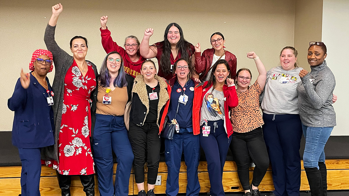 Large group of nurses inside hospital with raised fists smiling
