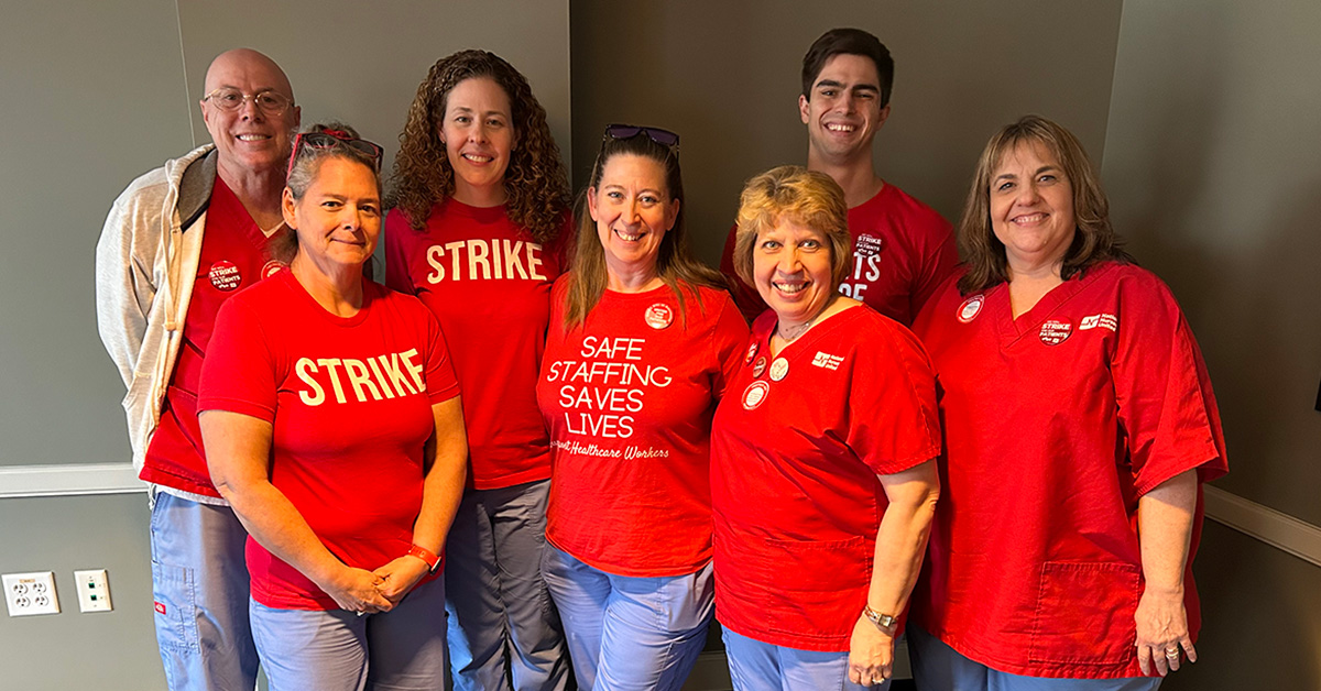 Group of seven nurses inside hospital smiling and wearing red