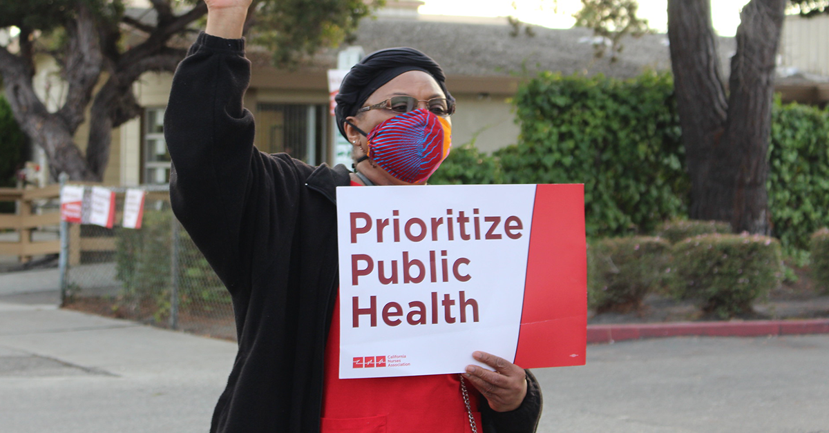 Nurse holds sign "Prioritize Public Health"