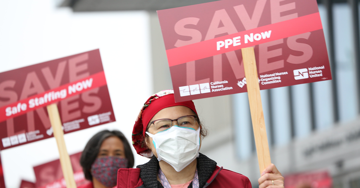 Nurse holds sign "PPE Now"