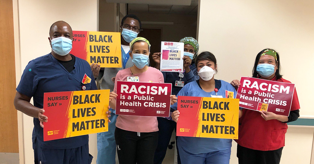 Group of nurses in hospital hold signs "Racism is a Public Health Crisis" and "Black Lives Matter"