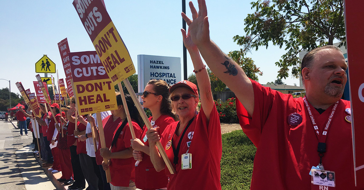 Nurses outside Hazel Hawkins Hospital hold signs "Some cuts don't heal"
