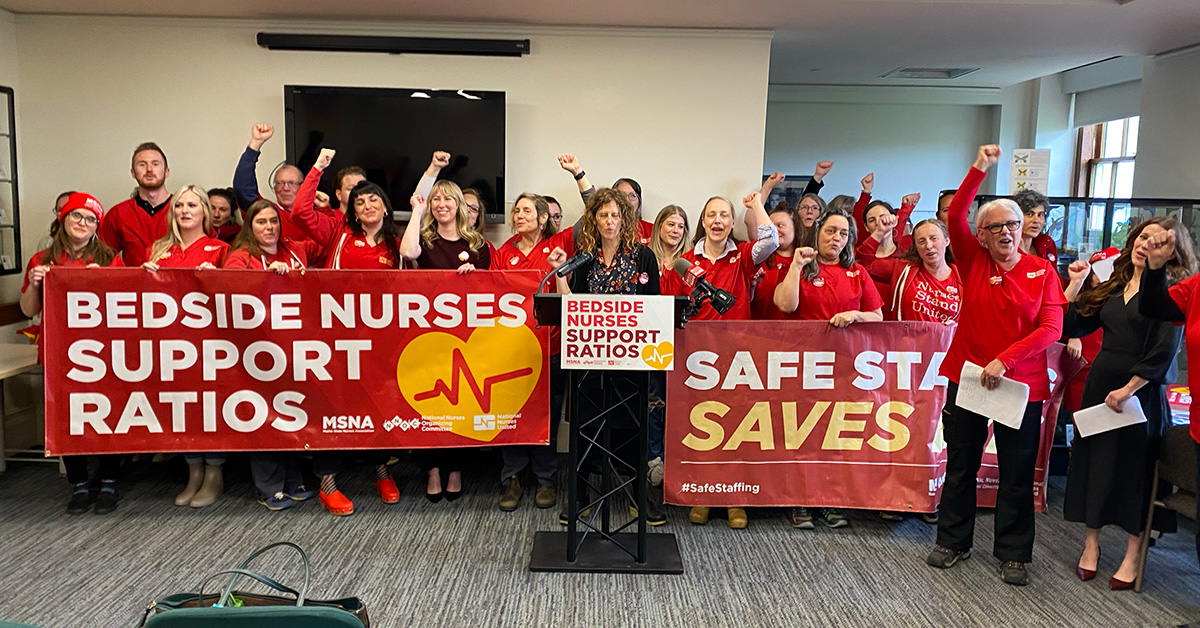 Large group of nurses with raised fists, holding banner "Bedside Nurses Support Ratios"