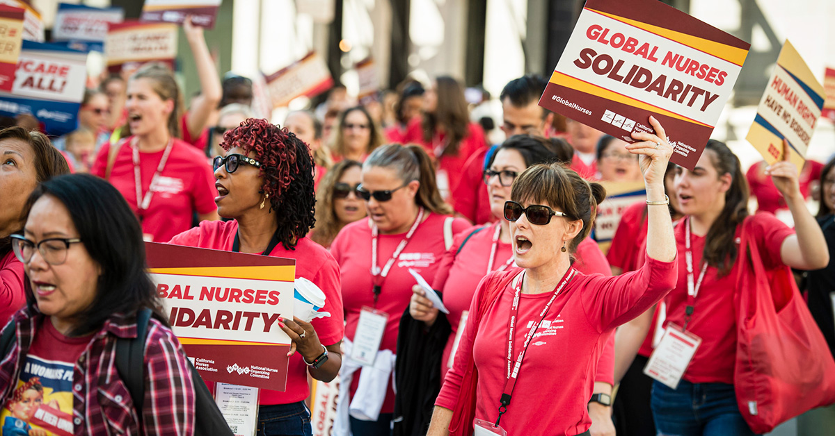 Nurses marching, holding signs "Global Nurses Solidarity"