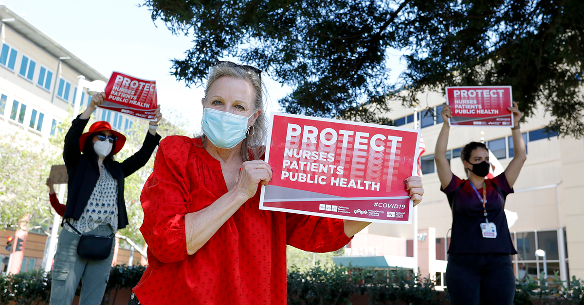 Nurses outside hospital hold signs "Protect Nurses, Patients, Public Health"