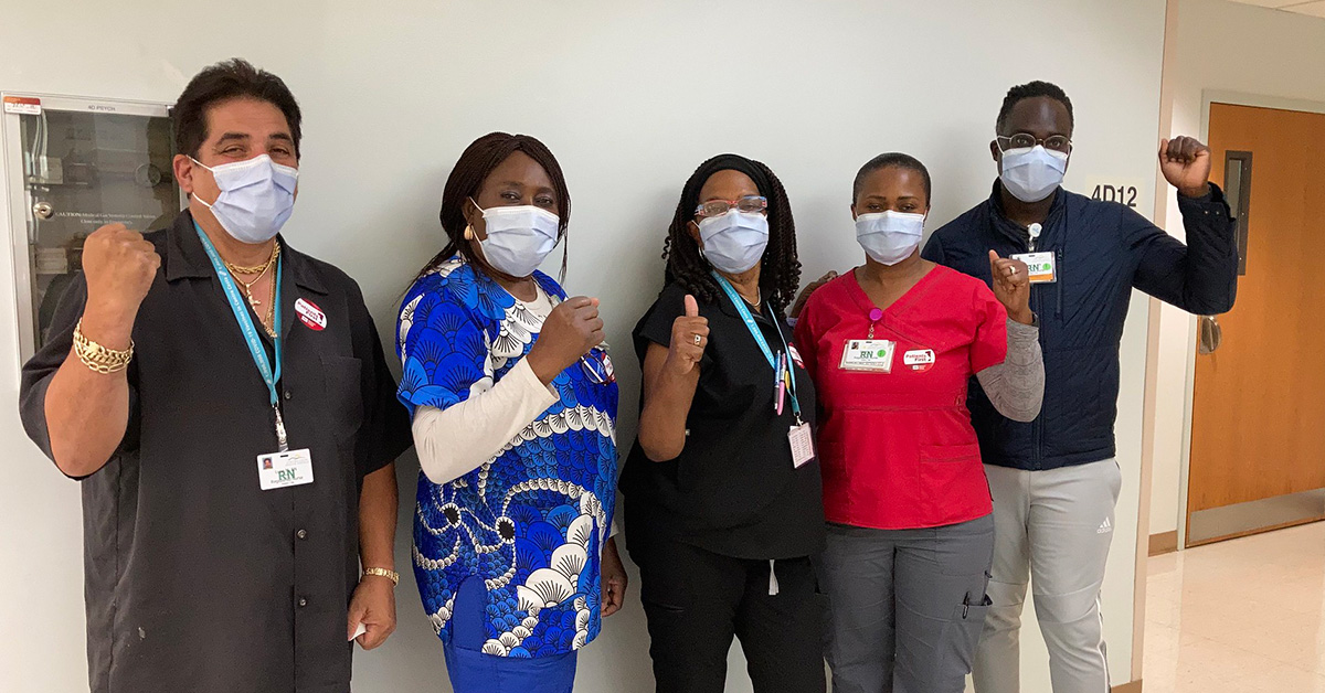 Group of five nurses inside hospital giving thumbs up