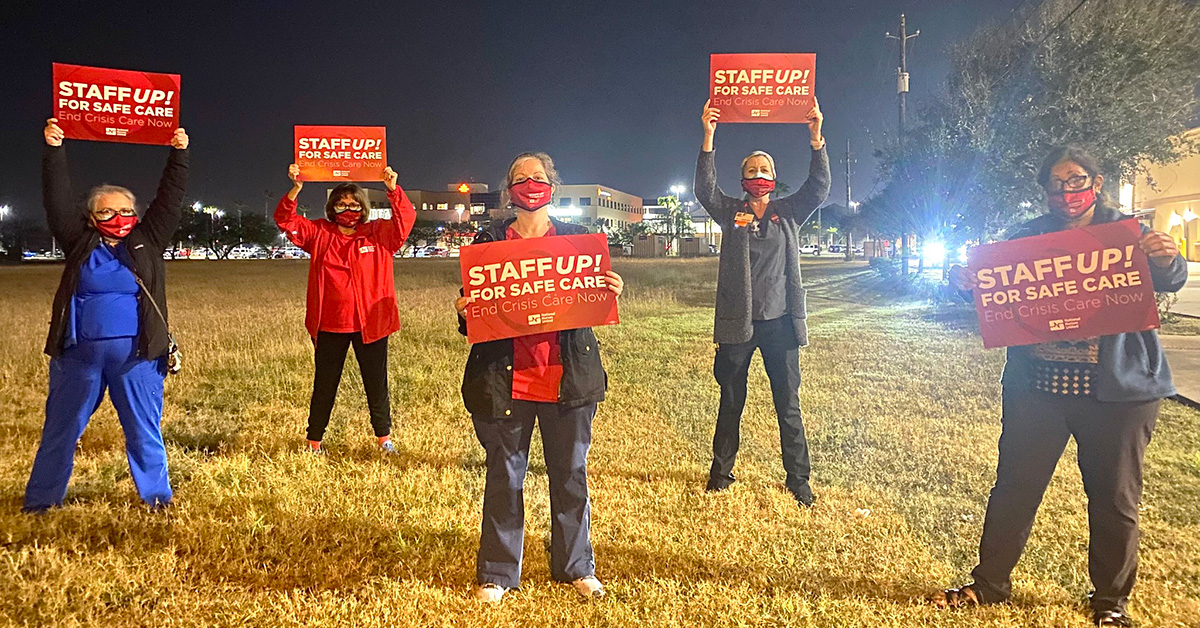 Group of nurses outside hold signs "Staff Up for Safe Care"