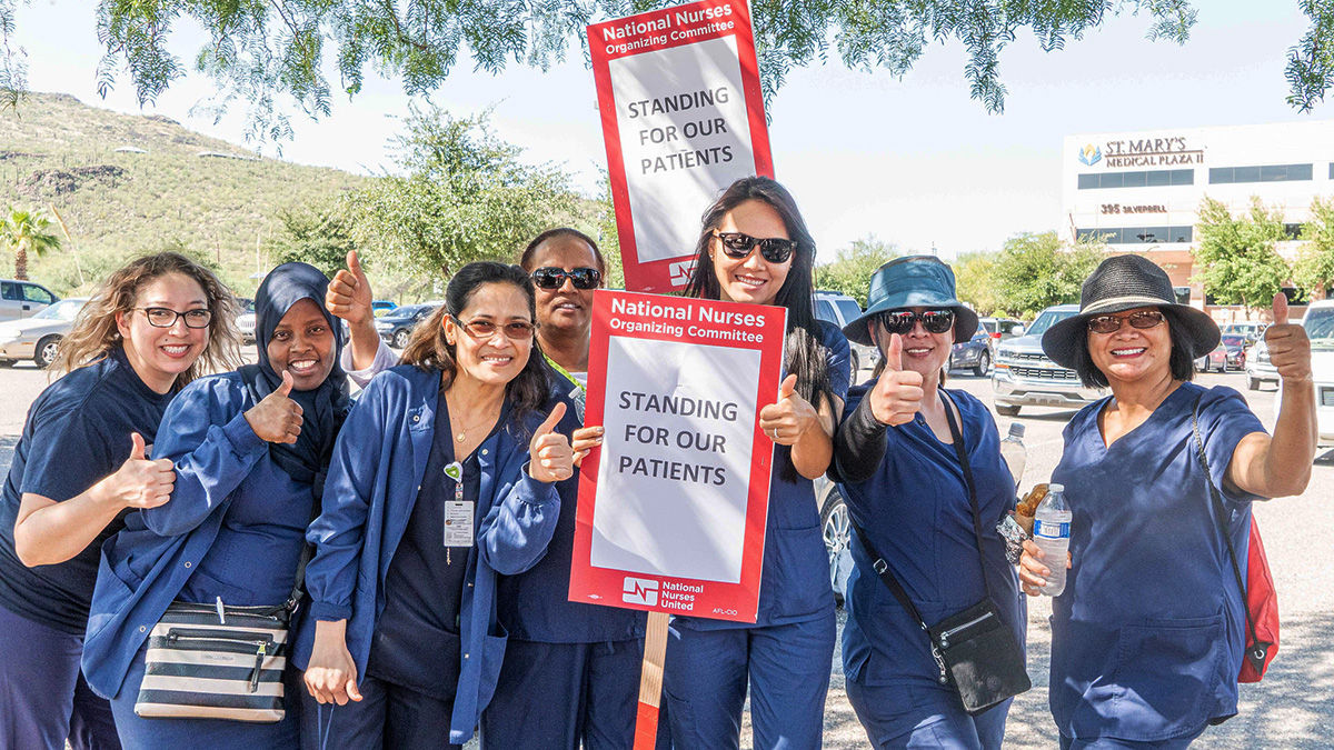Group of nurses outside hold sign "Standing for our patients"