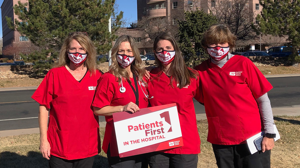 Group of four nurses outside hospital hold sign "Patients First"