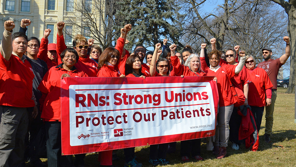 Large group of nurses hold banner "Strong Unions Protect Our Patients"