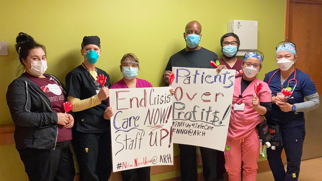 Group of nurses inside hospital hold signs "Patients Over Profits"