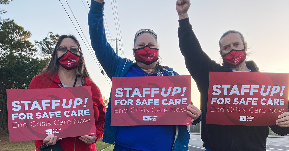 Three nurses outside with raised fists hold signs "Staff Up for Safe Care"