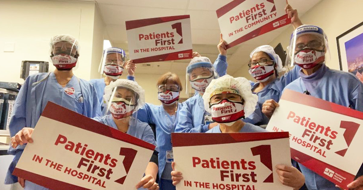 Large group of nurses inside hospital hold signs "Patients First"