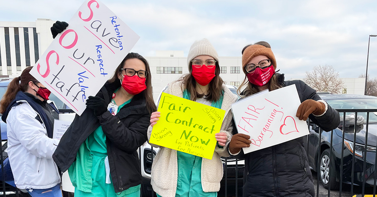 Three nurses outside holding signs "Save Our Staff", "Fair Contract Now", "Fair Bargaining"