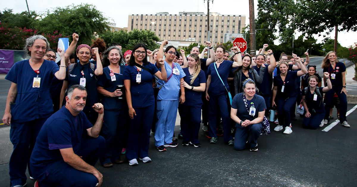 Large group of nurses outside hospital with raised fists