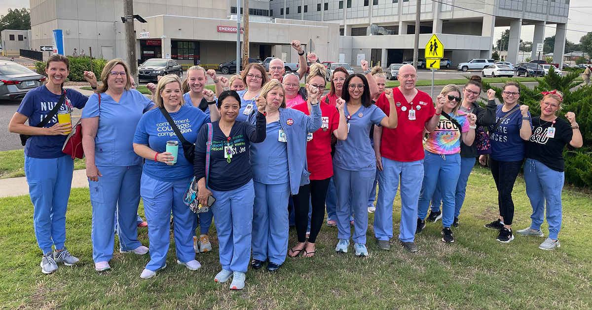 Large group of nurses outside hospital with raised fists