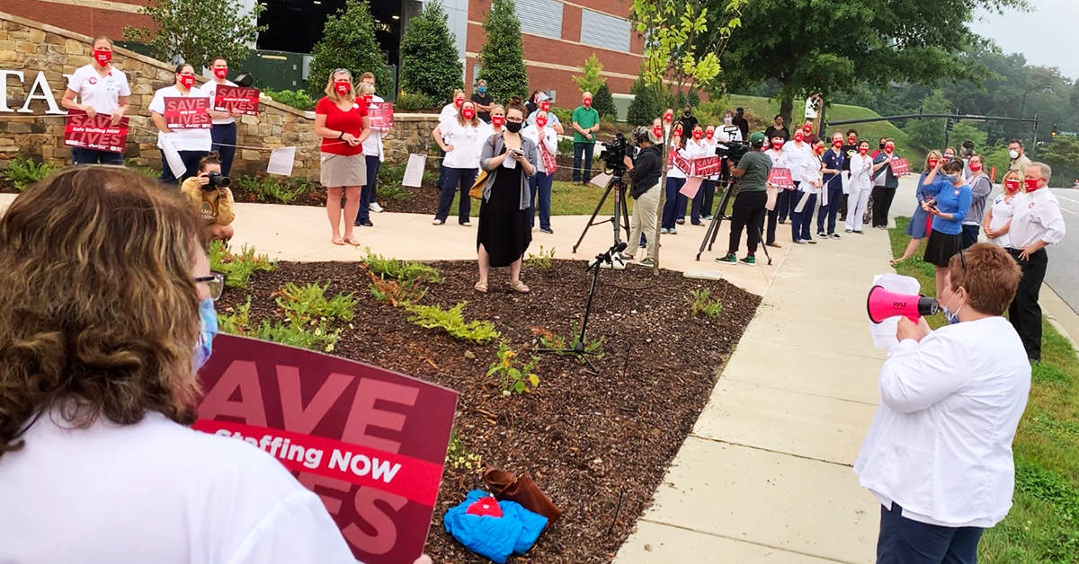 Nurses outside Mission facility holding event, sign in foreground "Save Lives, (Safe) Staffing Now"