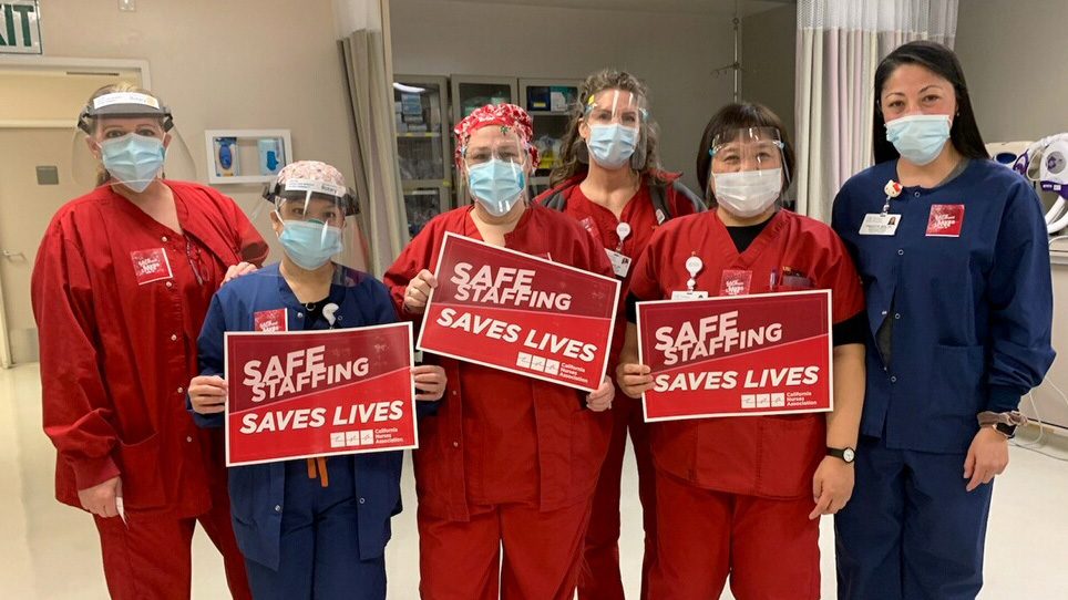 Group of nurses inside hospital hold signs "Safe Staffing Saves Lives"
