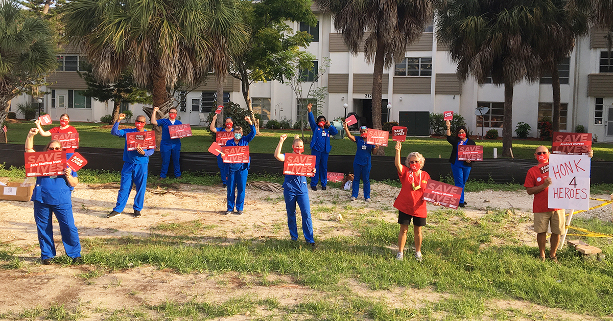 Nurses outside hospital holding various "Save Lives" signs