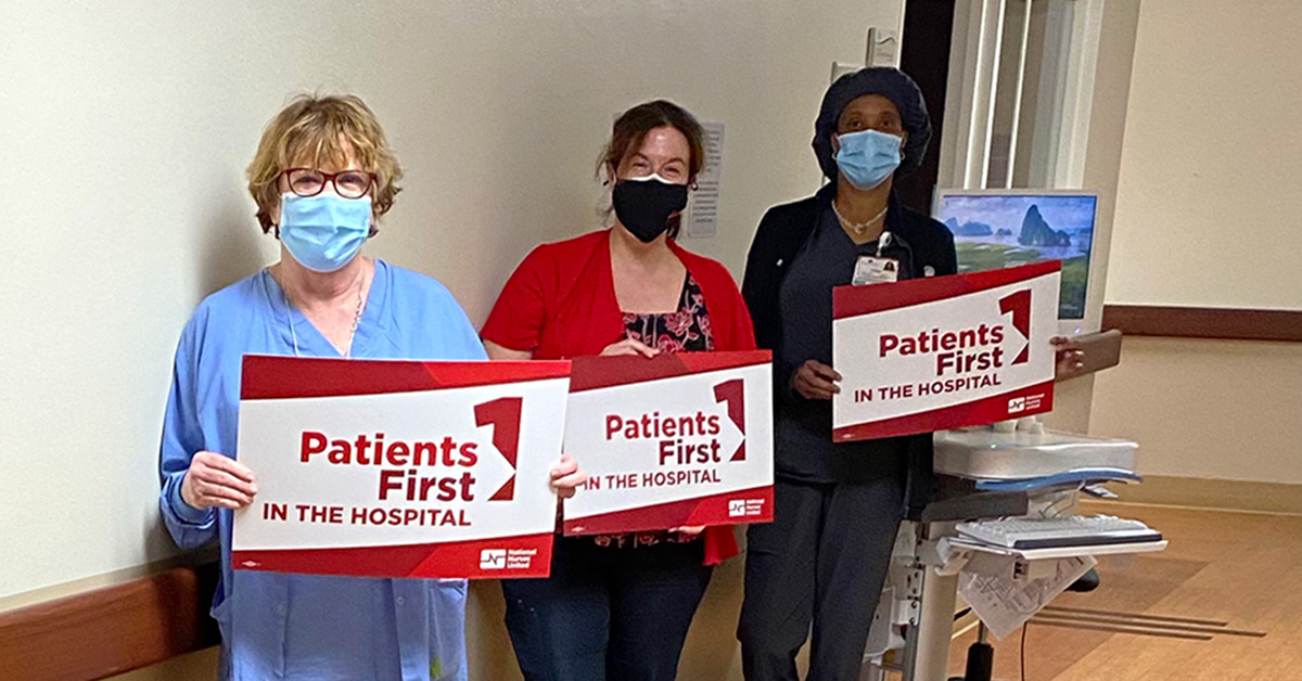 Three nurses inside hospital hold signs "Patients First"