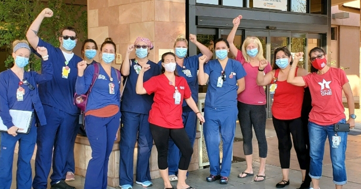 Large group of nurses outside hospital with raised fists