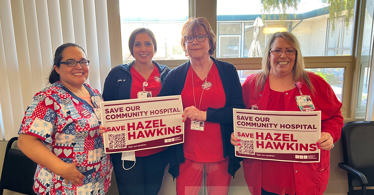 Group of four nurses inside hospital hold signs "Save Our Community Hospital: Save Hazel Hawkins"