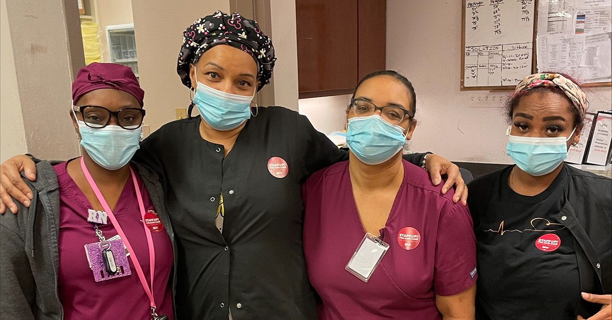 Four nurses inside hospital with arms around each other