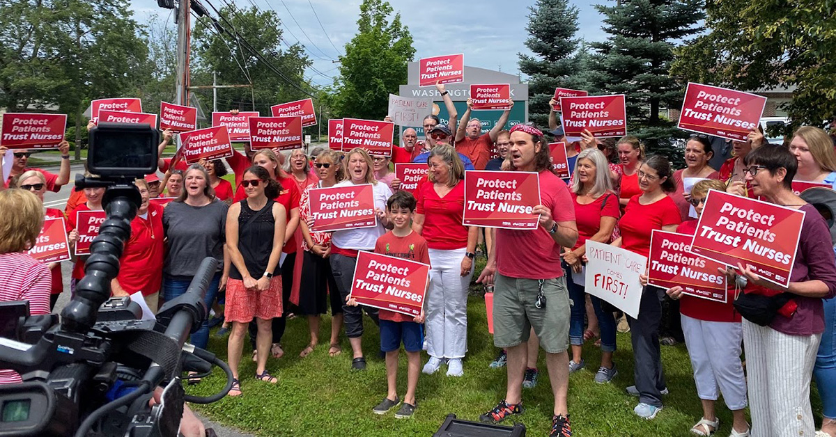 arge group of nurses in front of camera holding signs "Protect Patients, Trust Nurses"