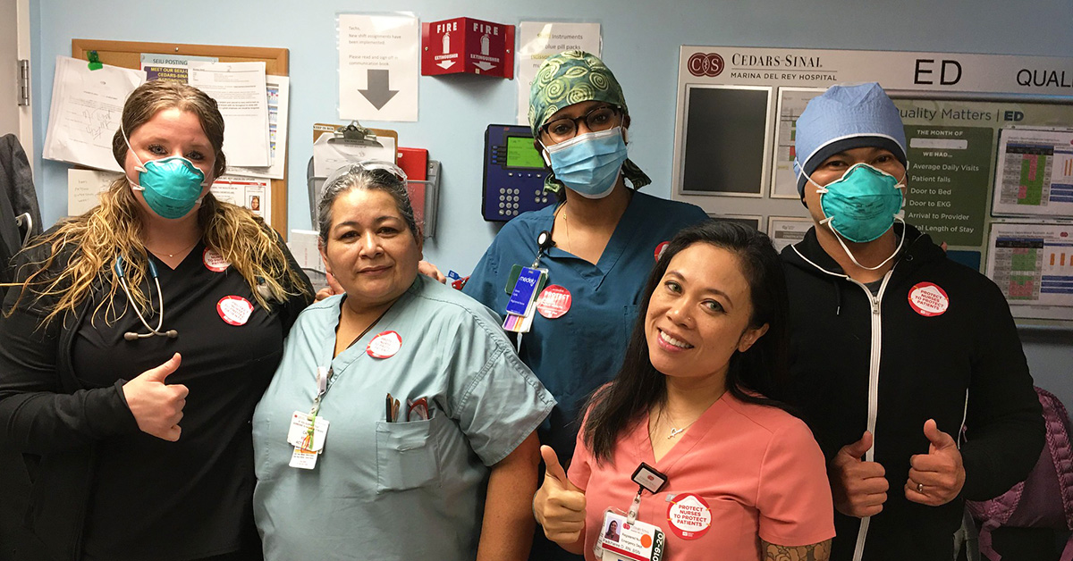 Group of five nurses inside hospital giving thumbs up