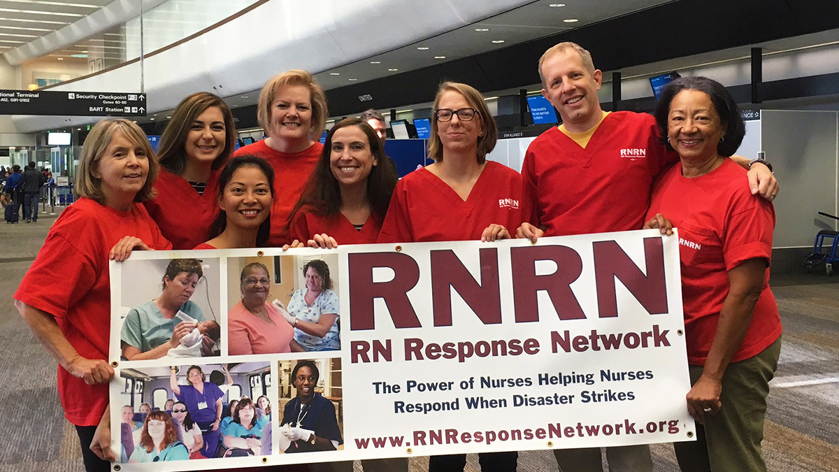 Group of nurses in airport in red scrub shirts holding RNRN banner